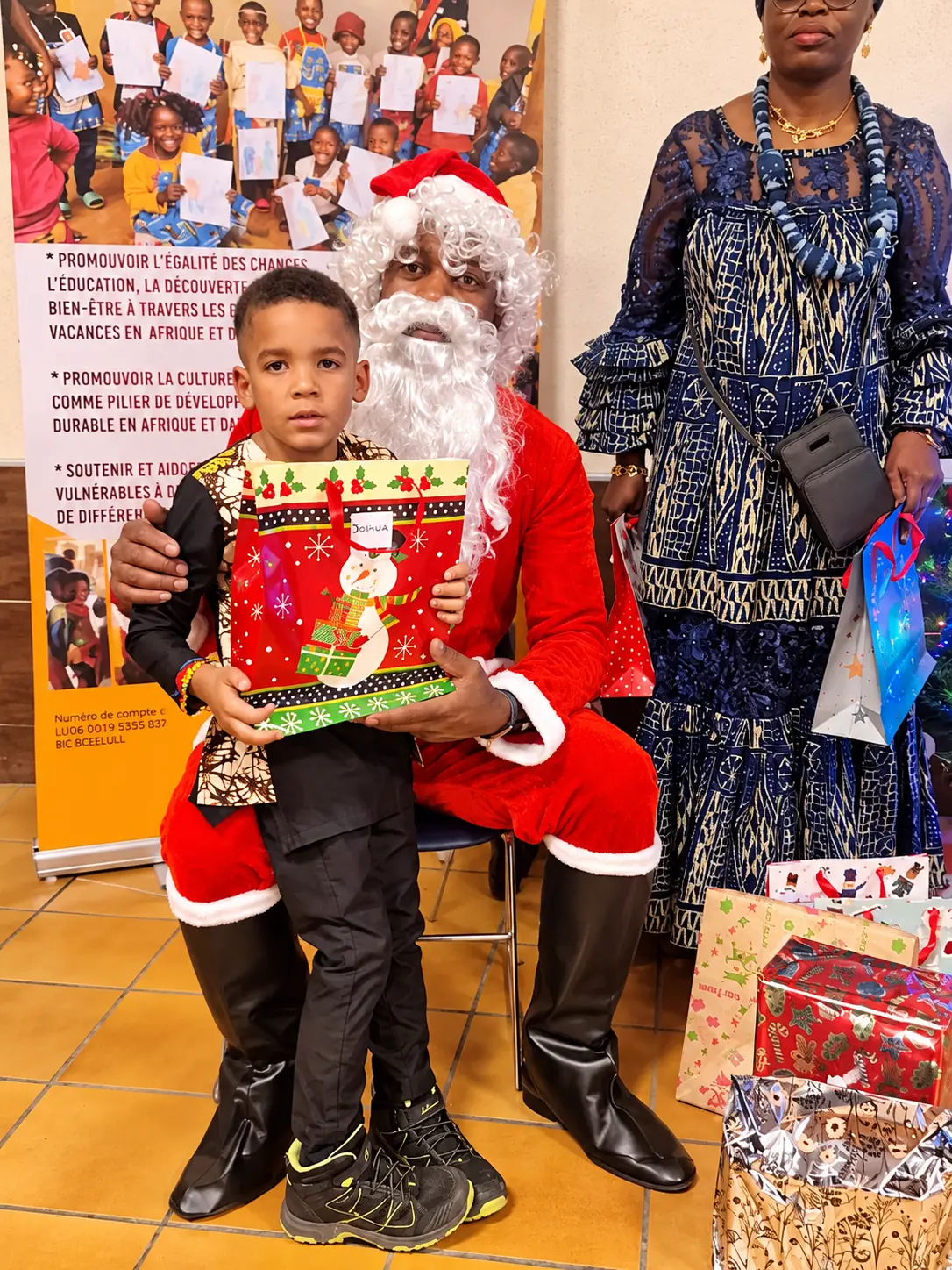 Le père Noël remettant un cadeau à un enfant devant les cadeaux